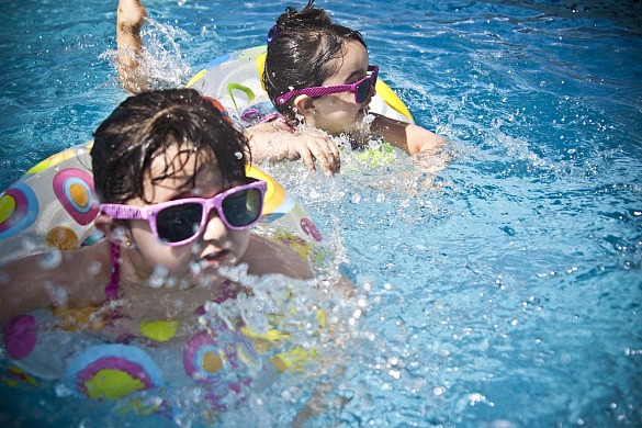 Das Bild zeigt zwei schwimmende Mädchen. Sie tragen eine Sonnenbrille und schwimmen mit Hilfe eines Schwimmringes. 
